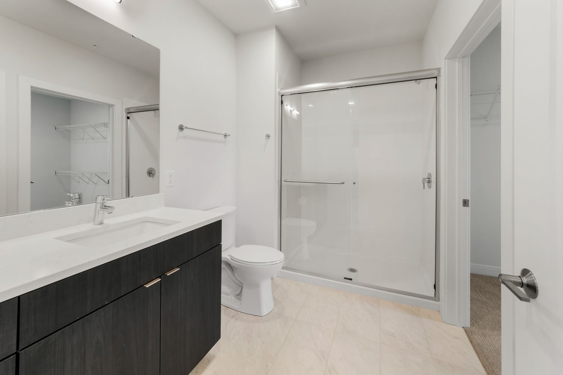 Modern white bathroom with a dark cabinet, glass shower, and toilet.