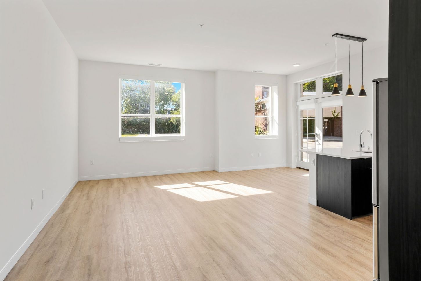 Empty modern living space with light wood floors, white walls, and large windows.