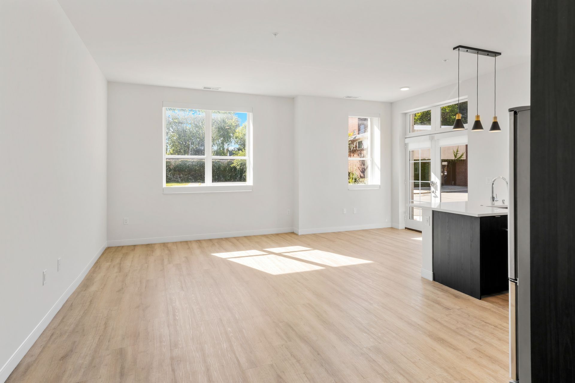 Empty modern living space with light wood floors, white walls, and large windows.