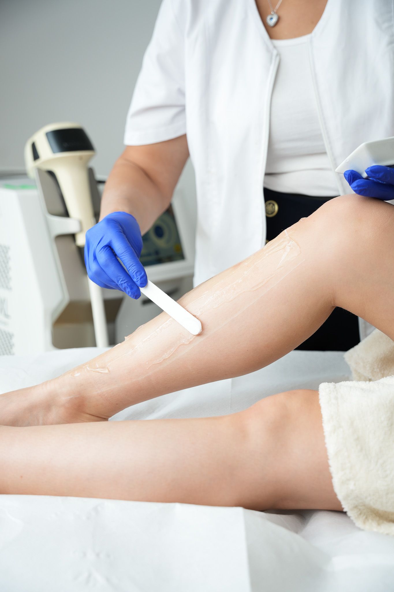Bein wird gewachst; eine Kosmetikerin mit Handschuhen trägt das Wachs mit einem Spatel auf.