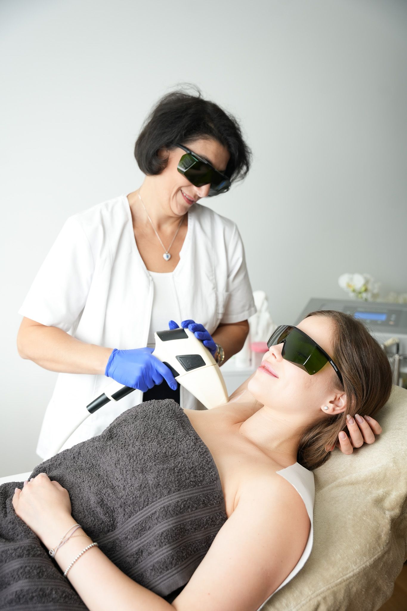 Eine Frau unterzieht sich einer Laserhaarentfernungsbehandlung durch eine Kosmetikerin; beide tragen eine Schutzbrille.