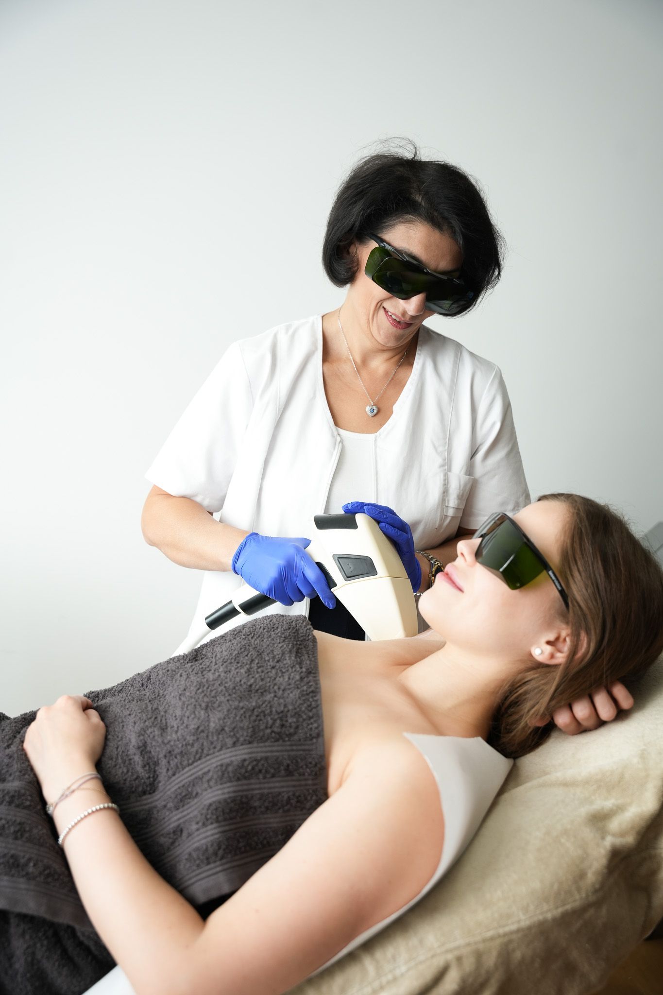 Eine Frau wird von einem Arzt am Hals mit Laser behandelt. Beide tragen in der medizinischen Umgebung eine Schutzbrille.