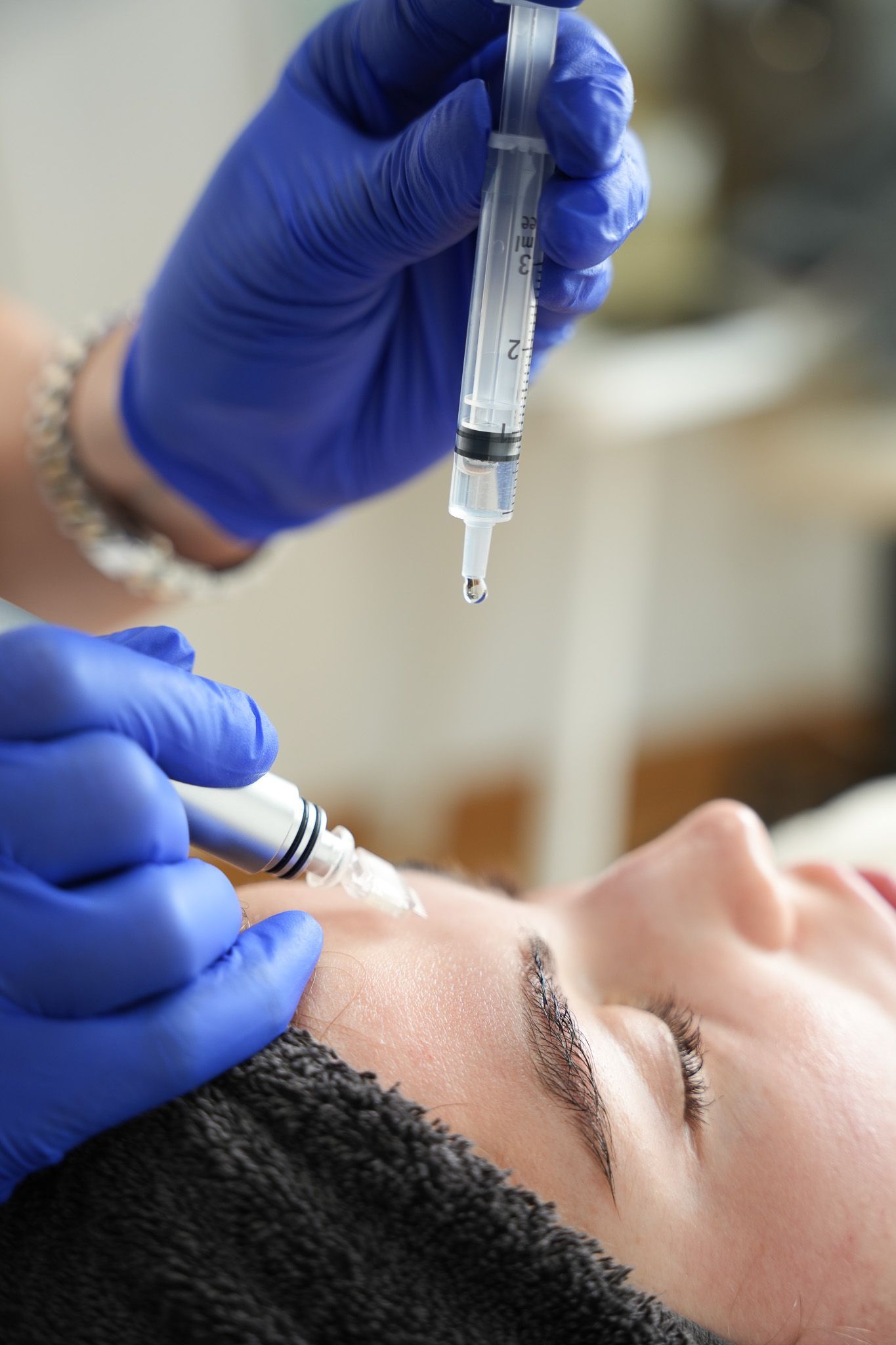 Person, die eine Gesichtsbehandlung erhält: Spritze, die Flüssigkeit auf die Haut abgibt, blaue Handschuhe.