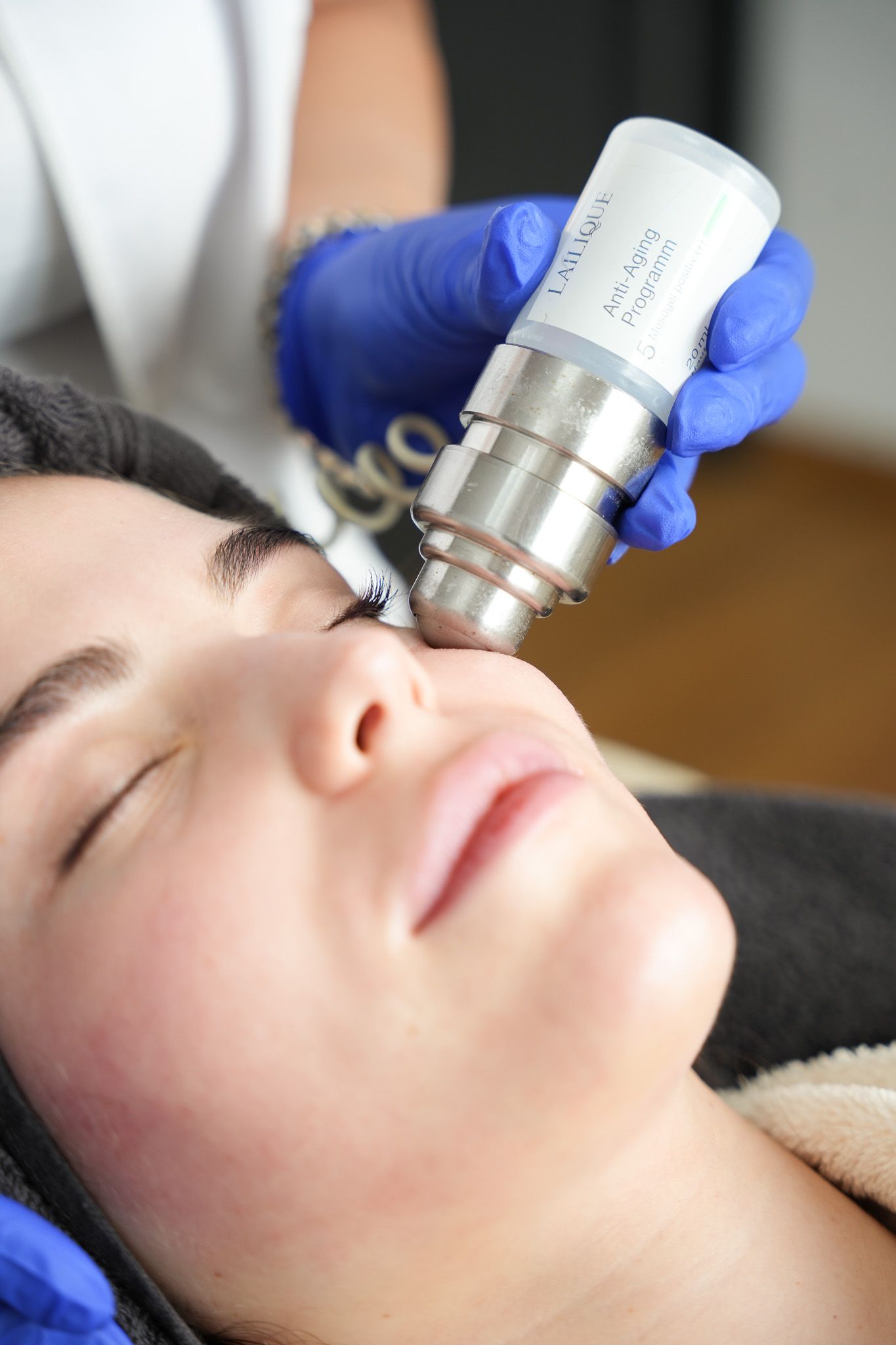 Frau erhält Gesichtsbehandlung mit einem Handgerät; Hand mit blauem Handschuh.