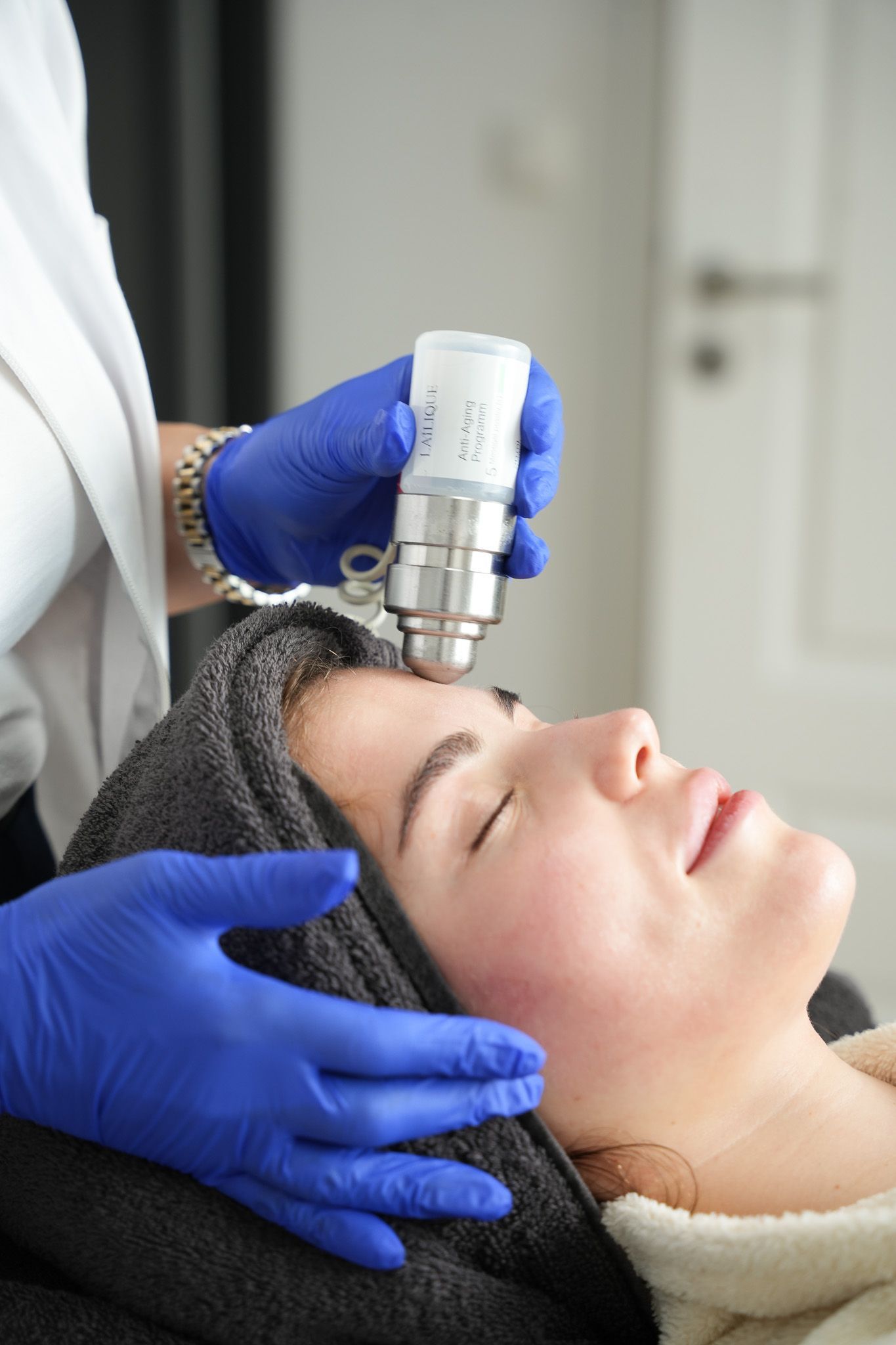 Person erhält eine Gesichtsbehandlung. Eine Kosmetikerin in blauen Handschuhen hält ein Gerät an die Stirn 