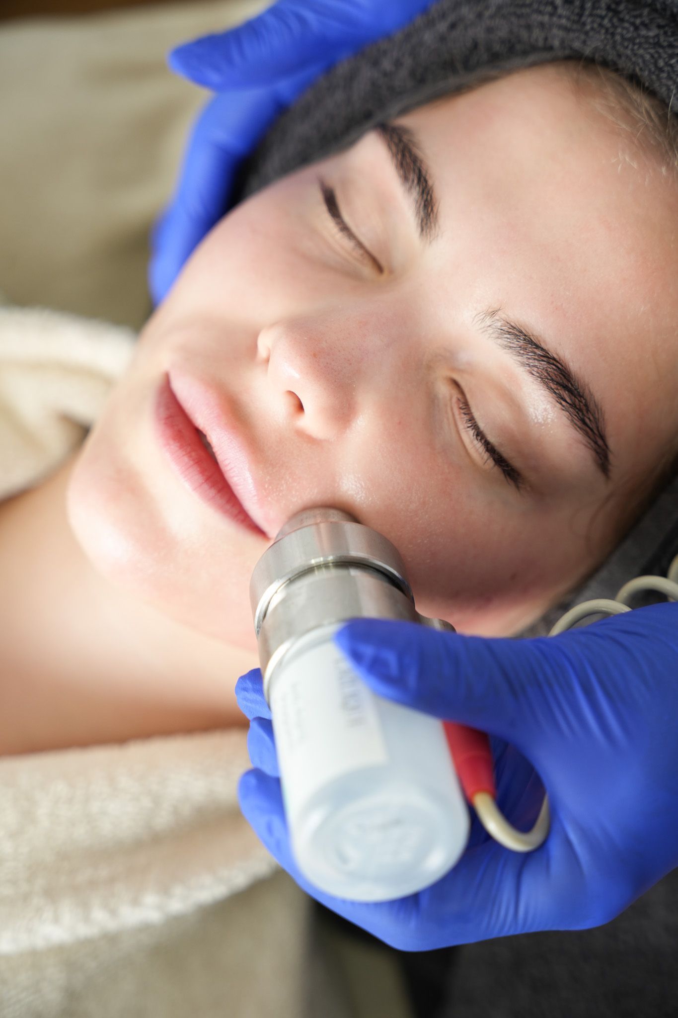 Eine Person erhält eine Gesichtsbehandlung. Eine behandschuhte Hand bedient ein Gerät im Gesicht.