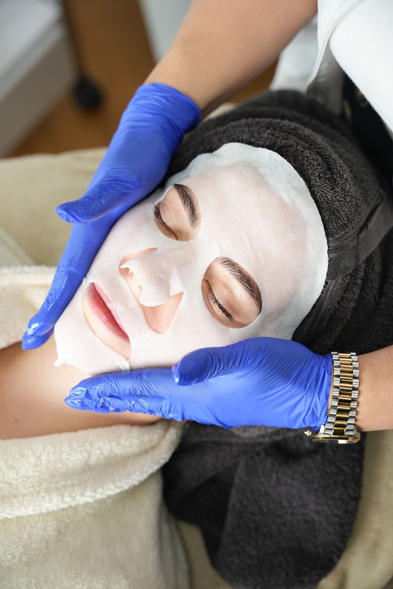 Eine Person mit einer Gesichtsmaske wird von behandschuhten Händen berührt.