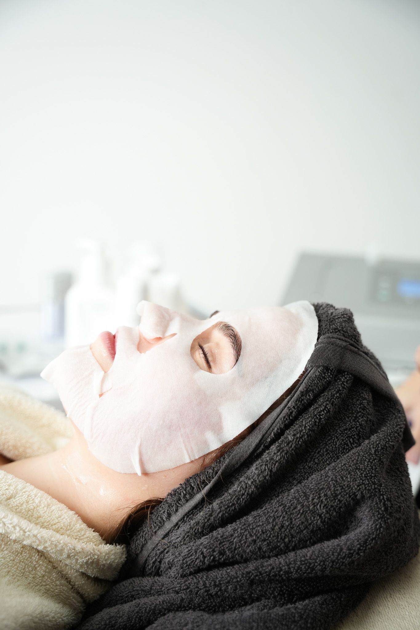 Eine Person mit einer Tuchmaske liegt mit einem Handtuch auf dem Kopf in einem Spa.