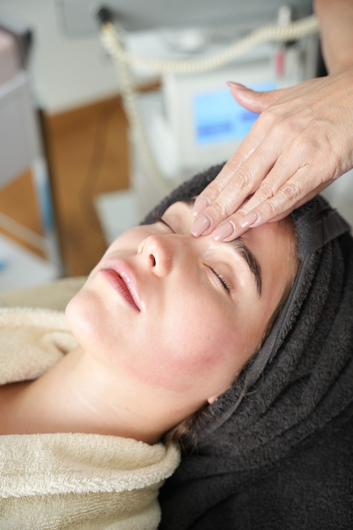 Eine Person erhält eine Gesichtsbehandlung, während die Hände die Stirn massieren; die Augen sind geschlossen.
