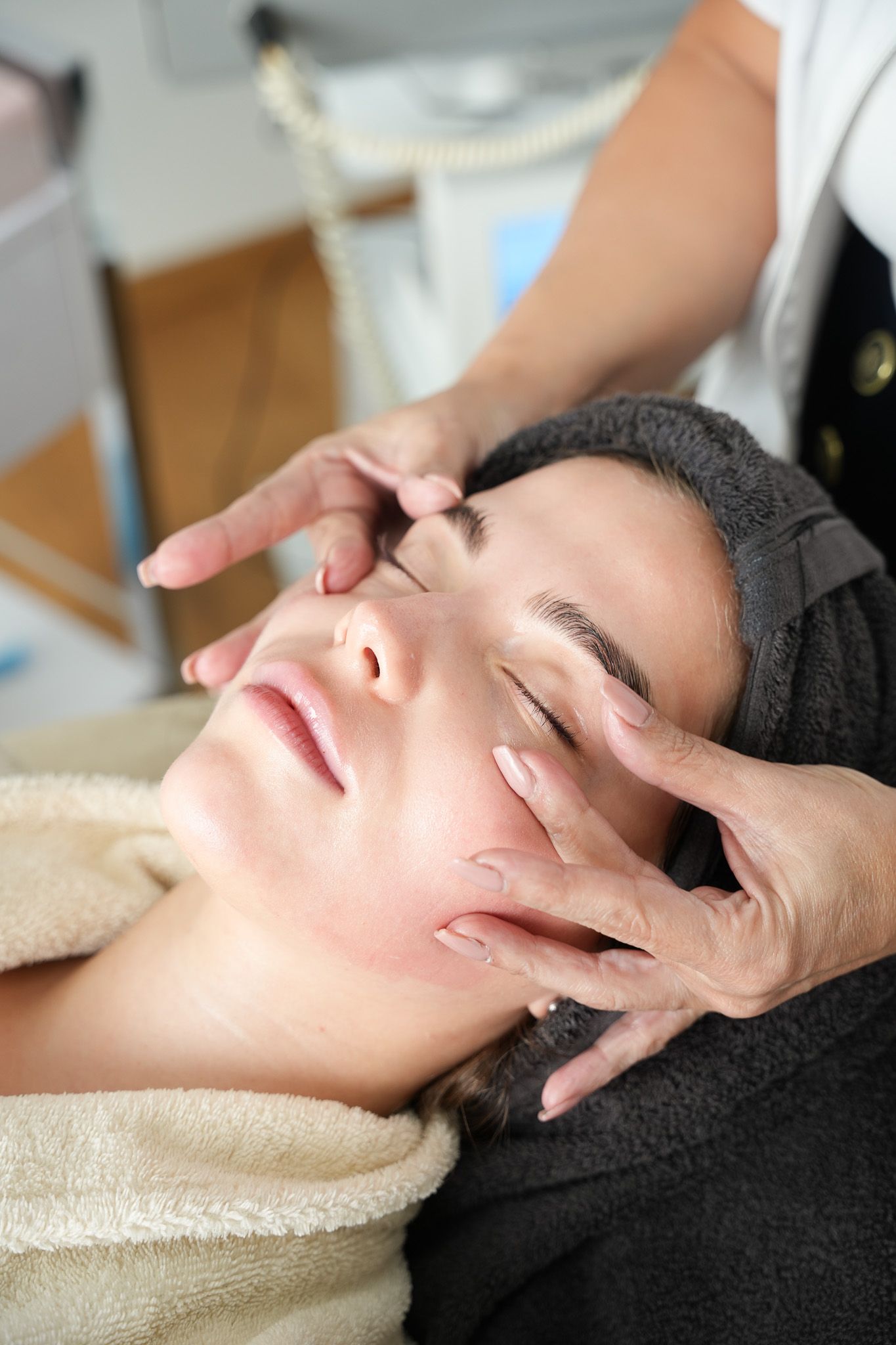 Eine Person genießt eine Gesichtsmassage in einem Spa; Hände an Wangen und Augen.