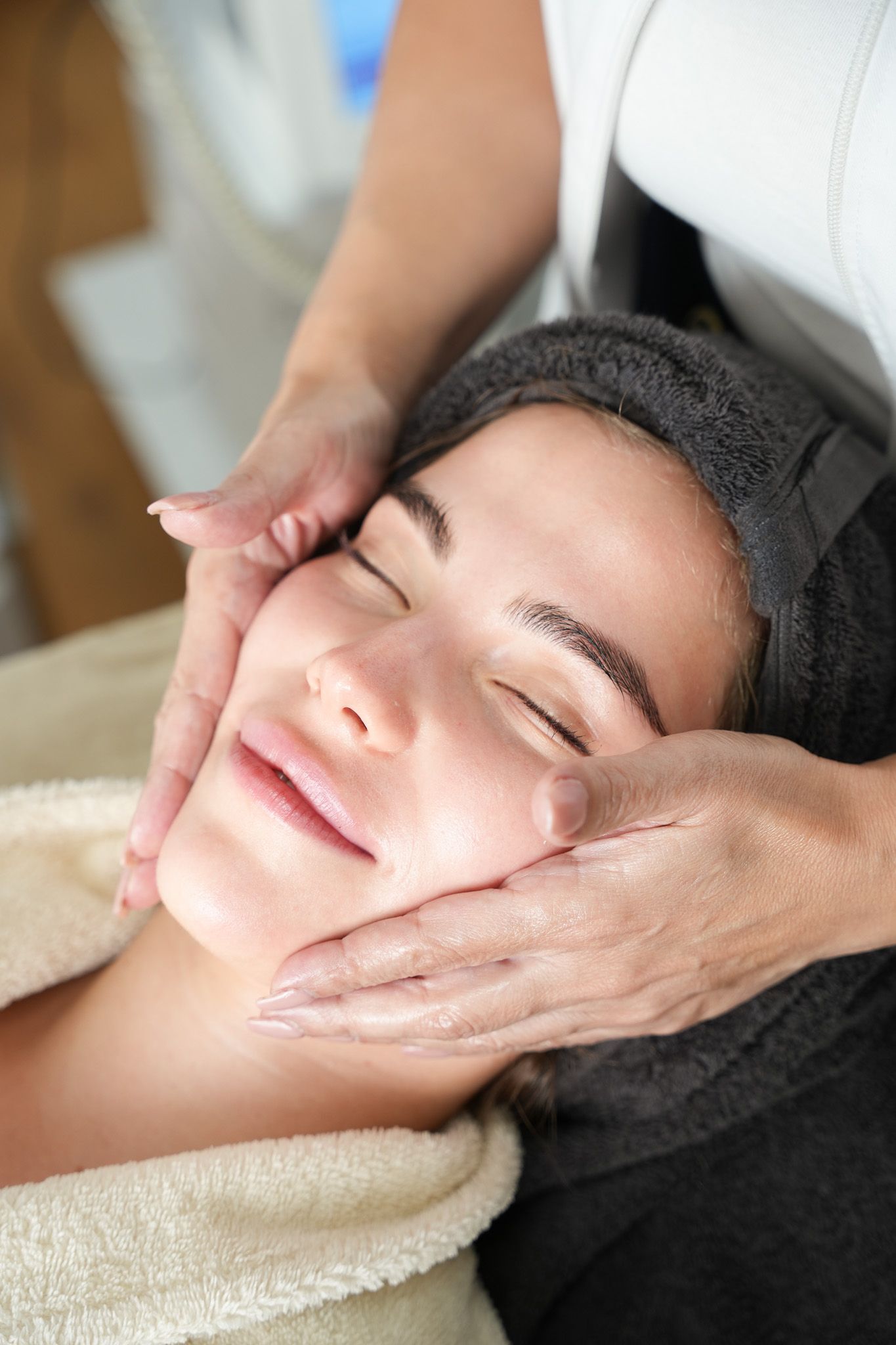 Eine Person, die in einem Spa eine Gesichtsmassage erhält; Hände an den Wangen, Augen geschlossen.