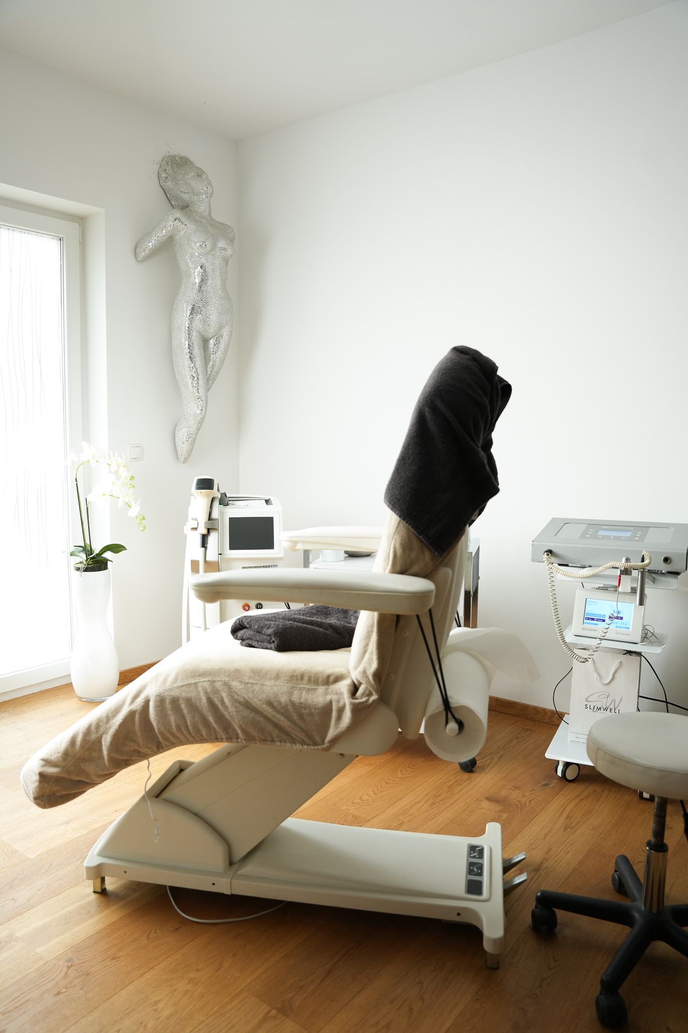 Medizinischer Untersuchungsraum mit verstellbarem Stuhl, Ausrüstung und einer dekorativen Figur an der Wand.