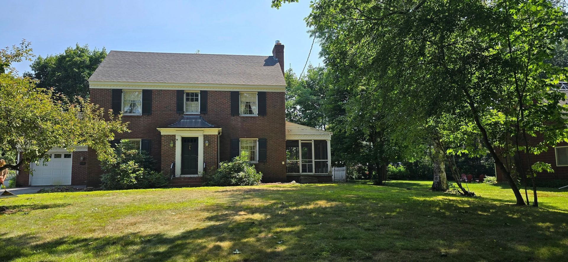 Brick two-story house with green lawn and trees on a sunny day.