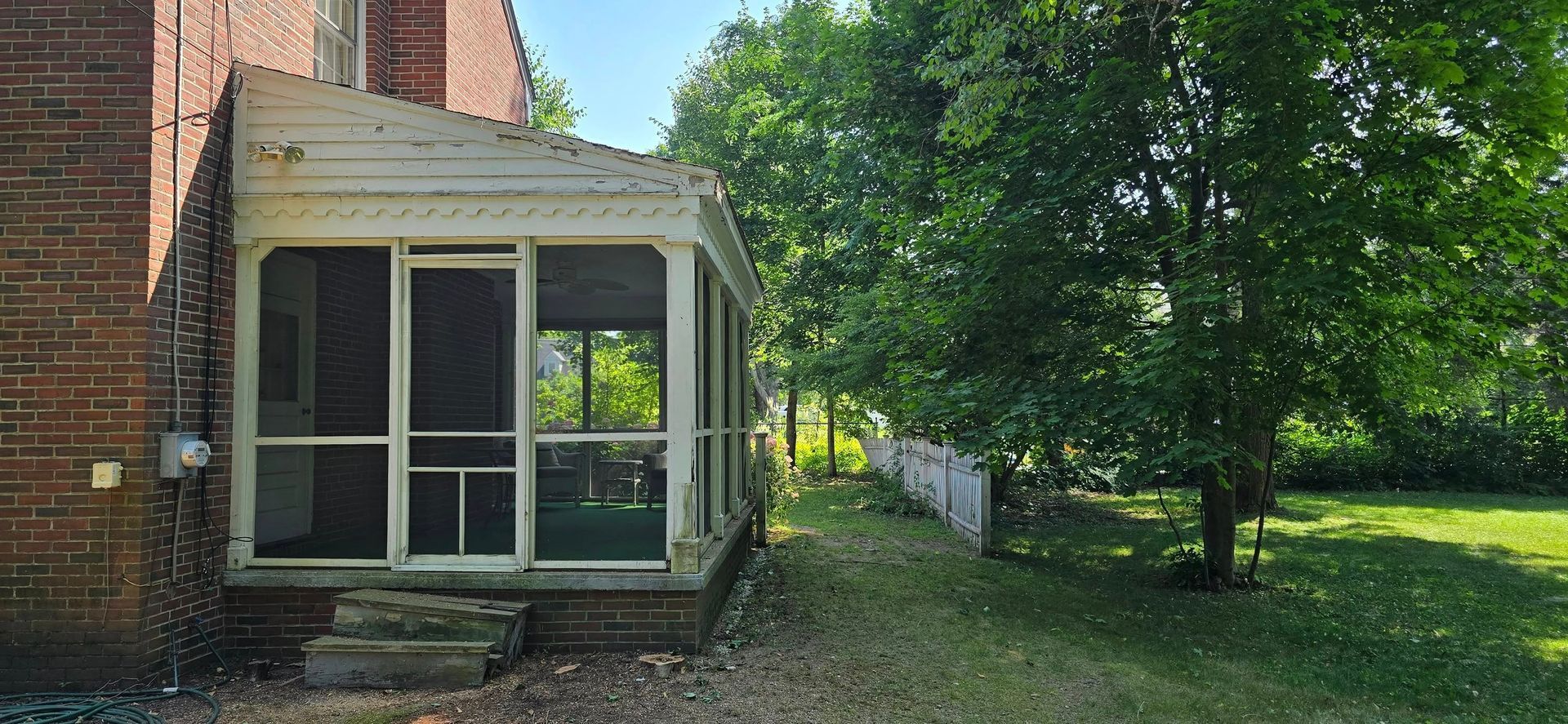 Screened porch attached to a brick house with a grassy backyard and a large tree.