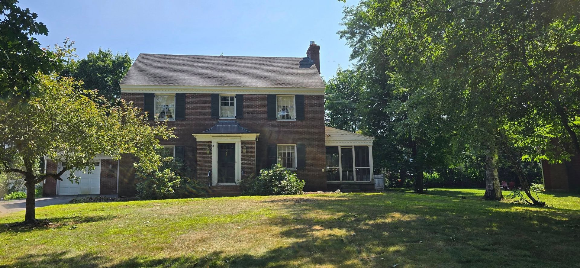 Two-story brick house with a green lawn and trees on a sunny day.
