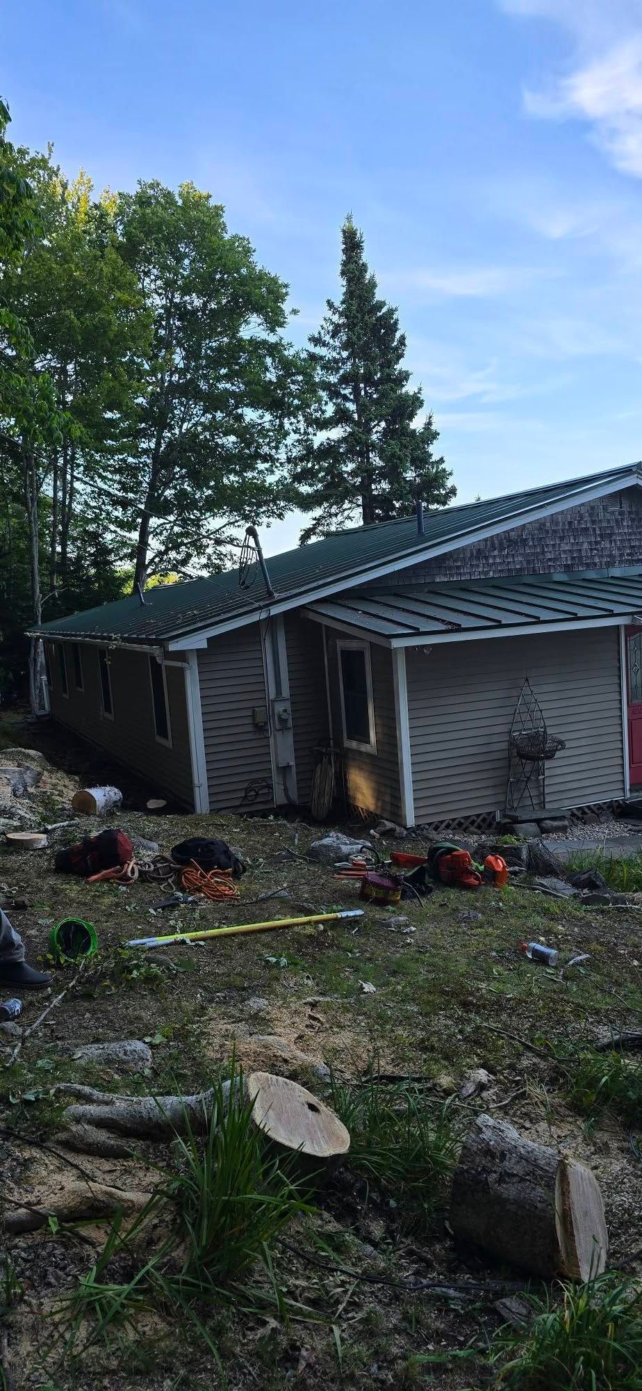 A fire-damaged house with charred door frame, surrounded by debris, trees, and blue sky.