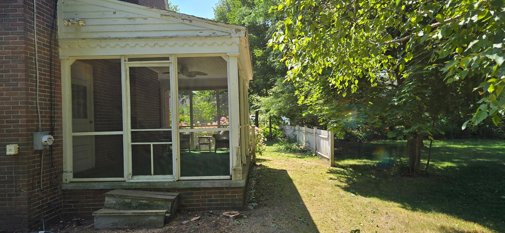A screened-in porch with brick steps next to a green yard and tree.