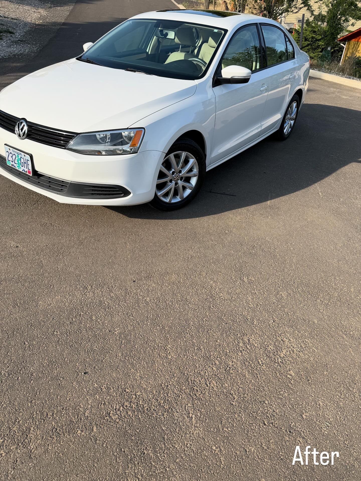 White sedan parked on a sunlit street near a stone wall