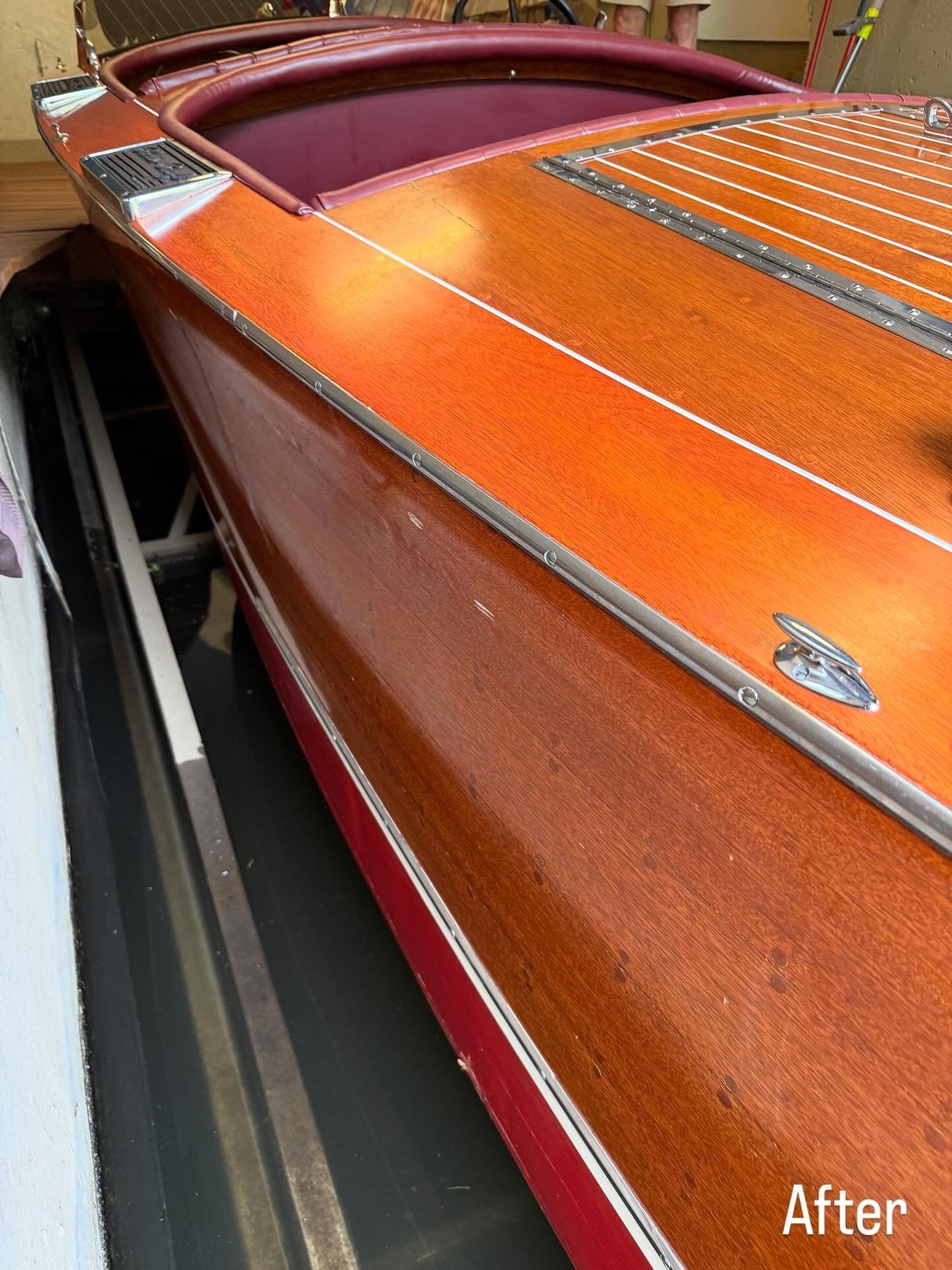 Close-up of a polished orange wooden boat hull with maroon trim in a narrow indoor storage space
