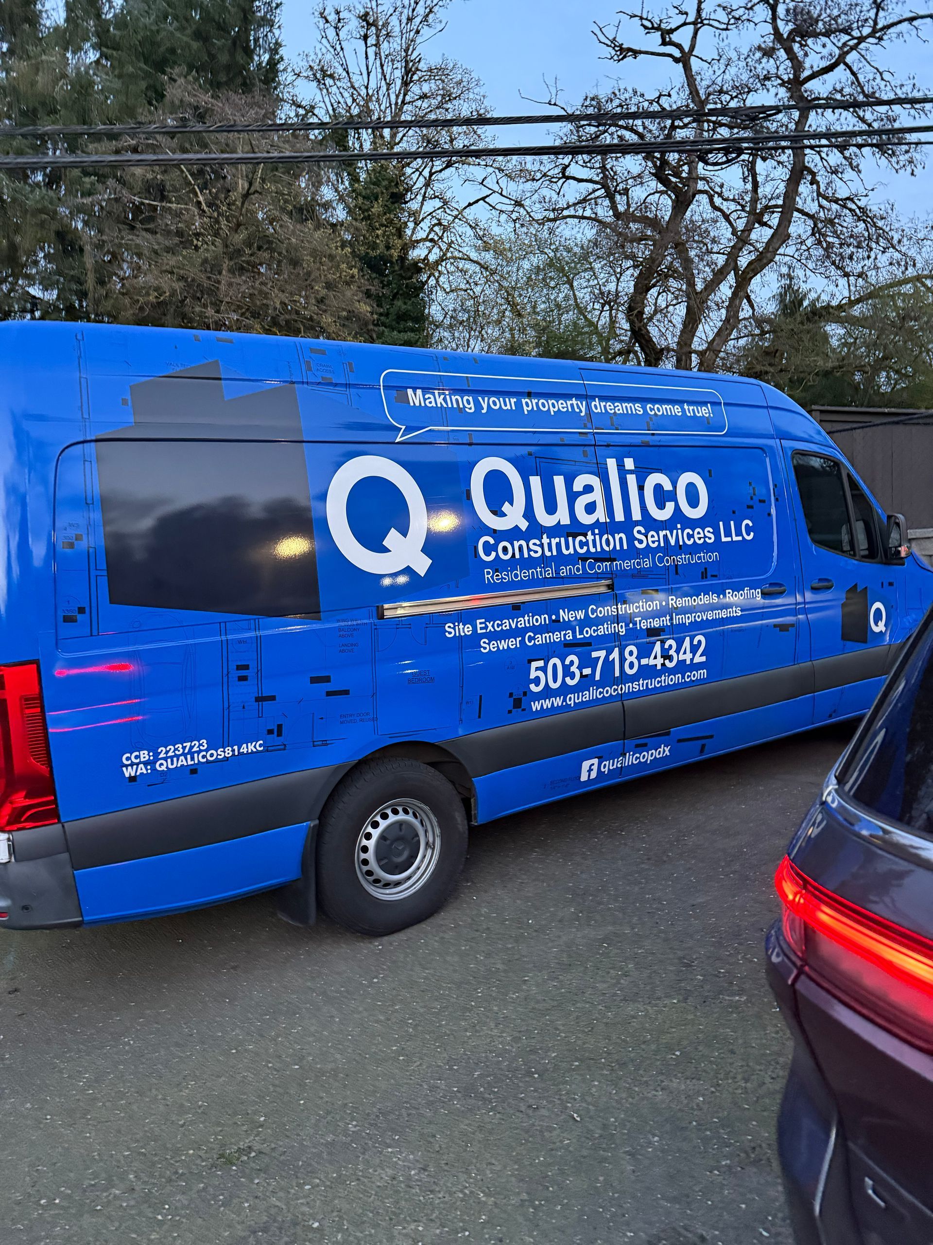 Blue Qualico Commercial Services van parked on a street beside other vehicles and trees.
