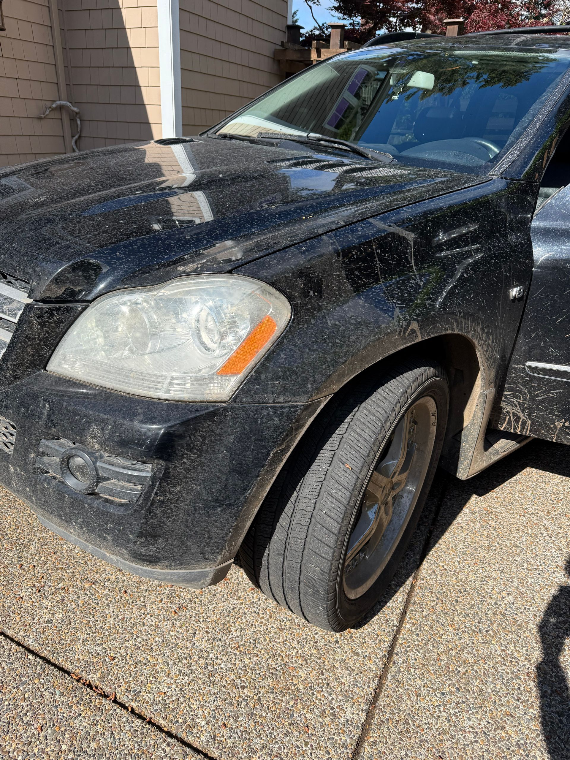 Black SUV parked on a gravel driveway beside a house, front-left view, dusty windshield and hood