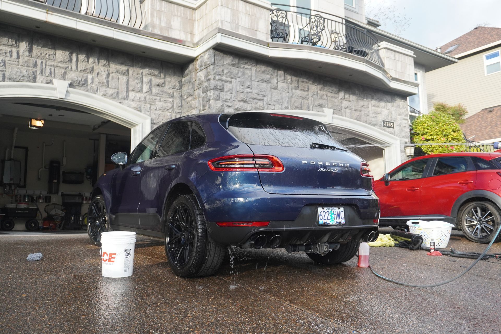Dark blue sedan being washed in a driveway, with soap buckets and a red car nearby.