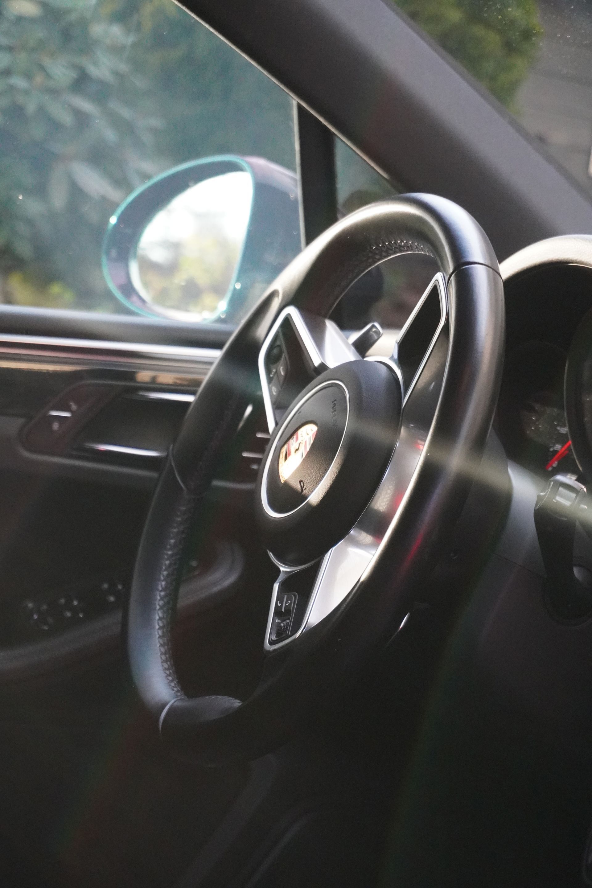 Car interior with black steering wheel and side mirror visible, parked outdoors in daylight