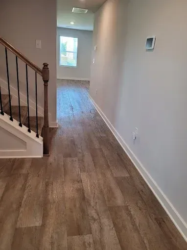 Entryway with wooden floor, staircase on the left, hallway, and light gray walls.