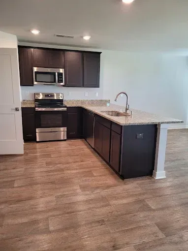Dark kitchen cabinets and island with granite countertops. Stainless steel appliances and wood-look flooring.
