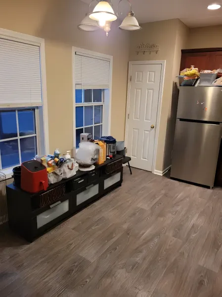 Kitchen with wood-look floor, two windows with blinds, a black cabinet with appliances, and a stainless steel refrigerator.