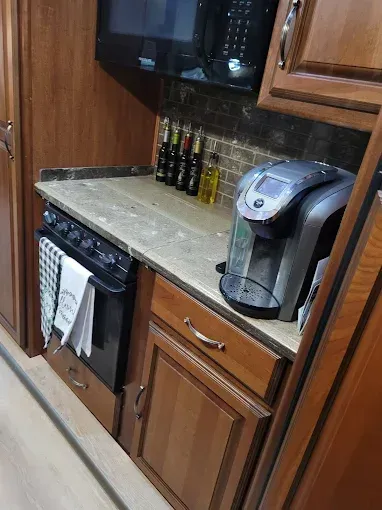 RV kitchen with stove, Keurig, countertop, and cabinets in shades of brown.