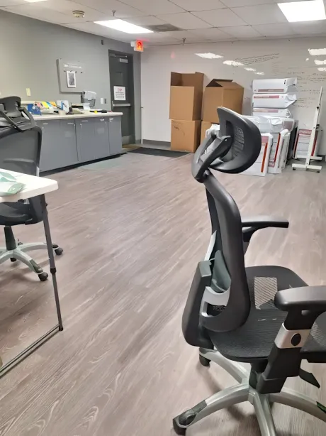Office space with ergonomic chair, gray cabinets, cardboard boxes, and wood-look flooring.