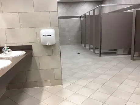 Public restroom with stalls and sinks. Beige tile, brown countertops, and white paper towel dispenser.