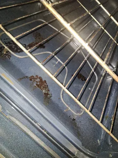 Inside of an oven with a wire rack, showing burnt food and rust on the interior.
