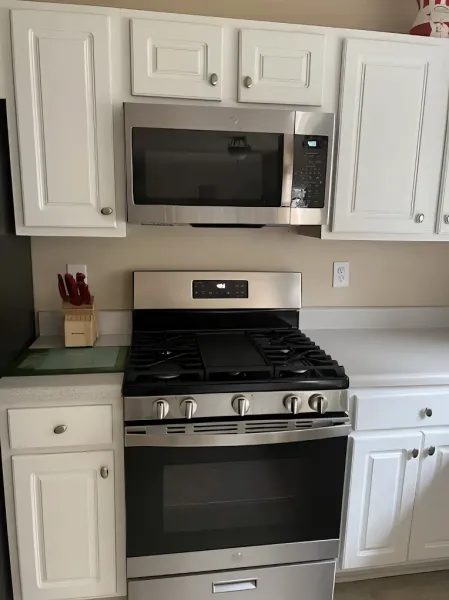 White kitchen cabinets surround a stainless steel microwave and gas range.