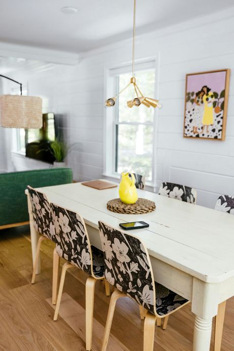 Dining area with white table, floral print chairs, yellow pear, artwork, window.