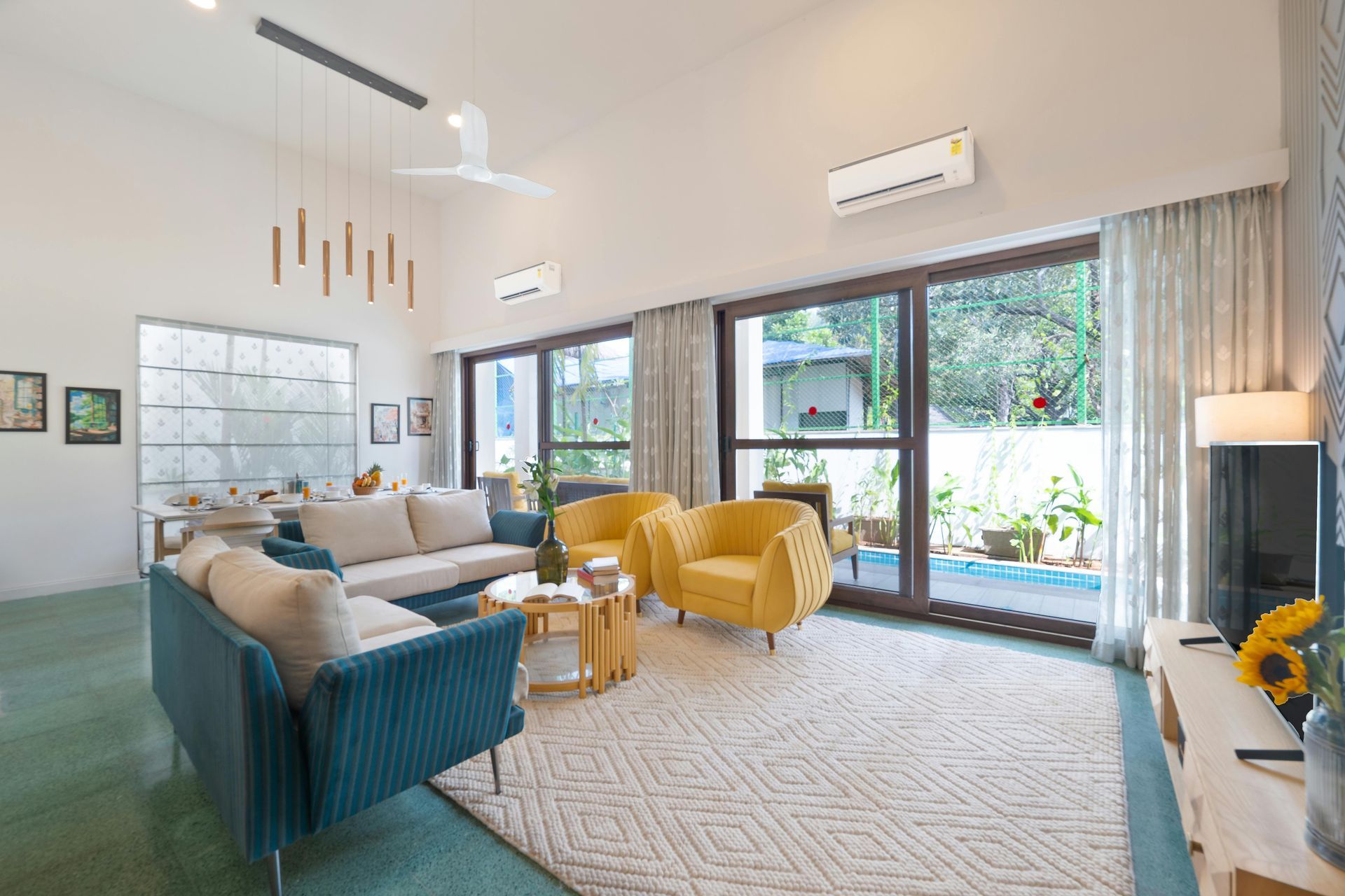 Bright living room with teal and yellow seating, large windows, and a patterned rug.
