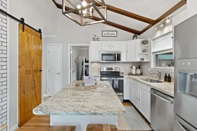 Kitchen with white cabinets, wood beams, granite island, stainless appliances, and a sliding barn door.