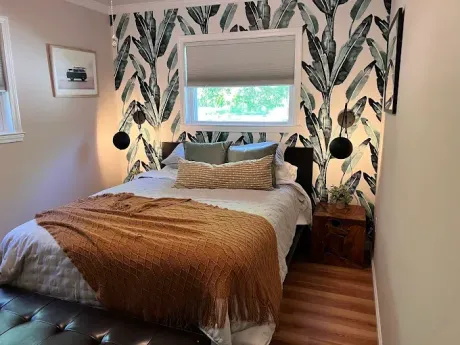 Bedroom with floral wallpaper, bed with brown throw, and two sconce lights.