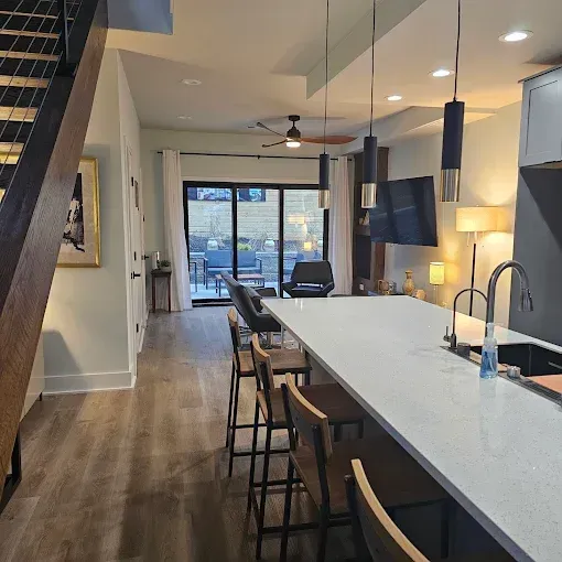 Modern kitchen with a long island, bar stools, and a view to a living area with sliding doors to a patio.