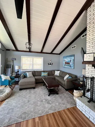 Living room with a gray sectional sofa, brick fireplace, wooden beams, and a patterned rug.