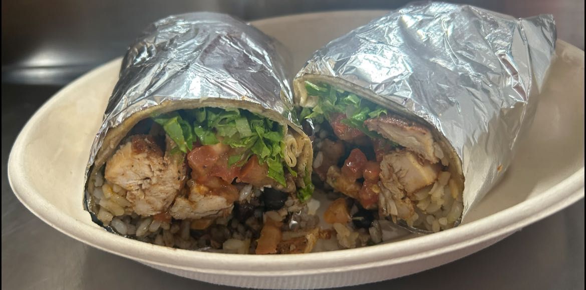 Two burritos wrapped in foil in a white bowl. Cut ends show chicken, tomatoes, lettuce, and rice.