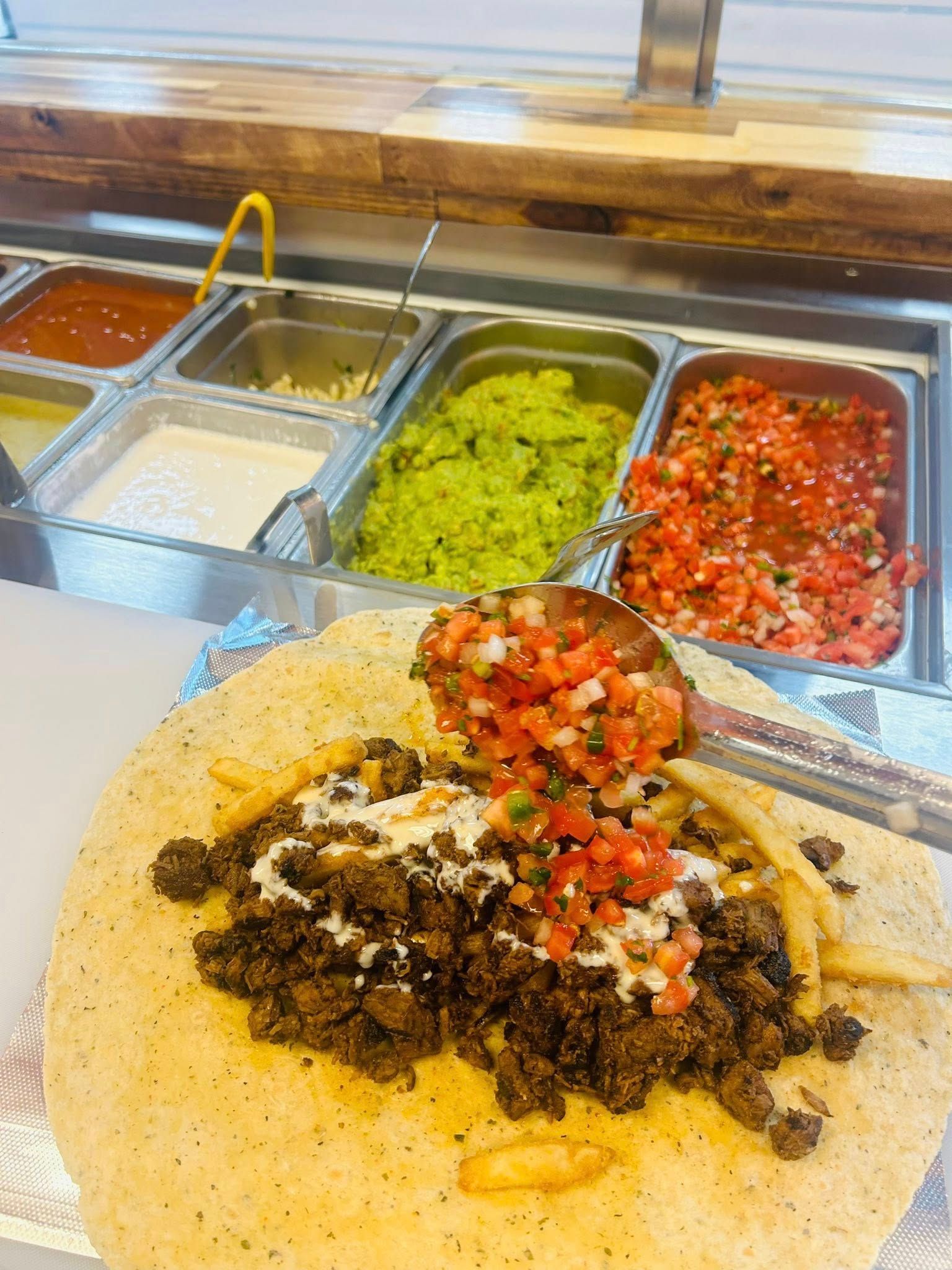 Burrito being prepared with toppings, including salsa and guacamole, at a restaurant.