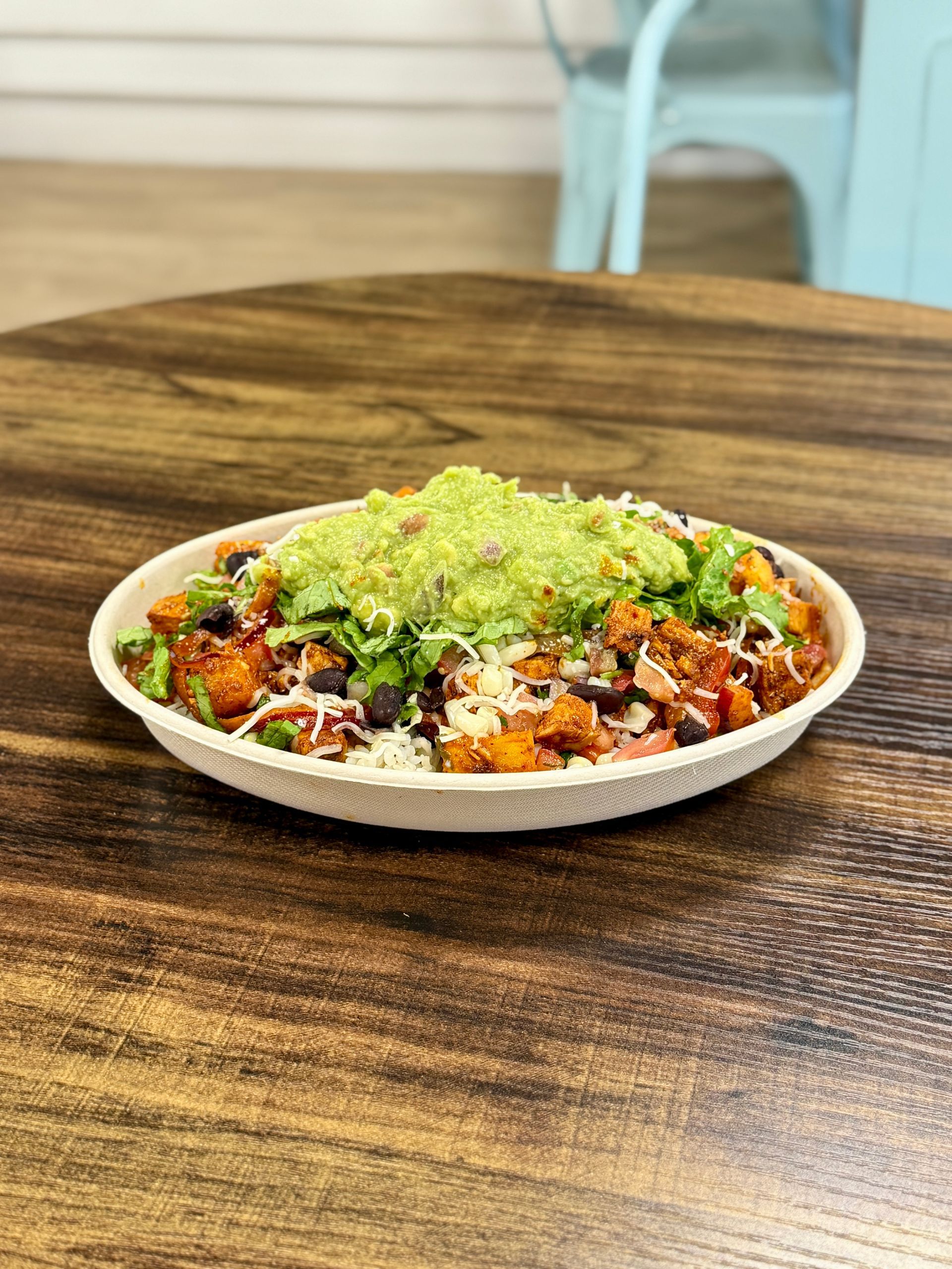Bowl of food with guacamole topping on a wooden table.