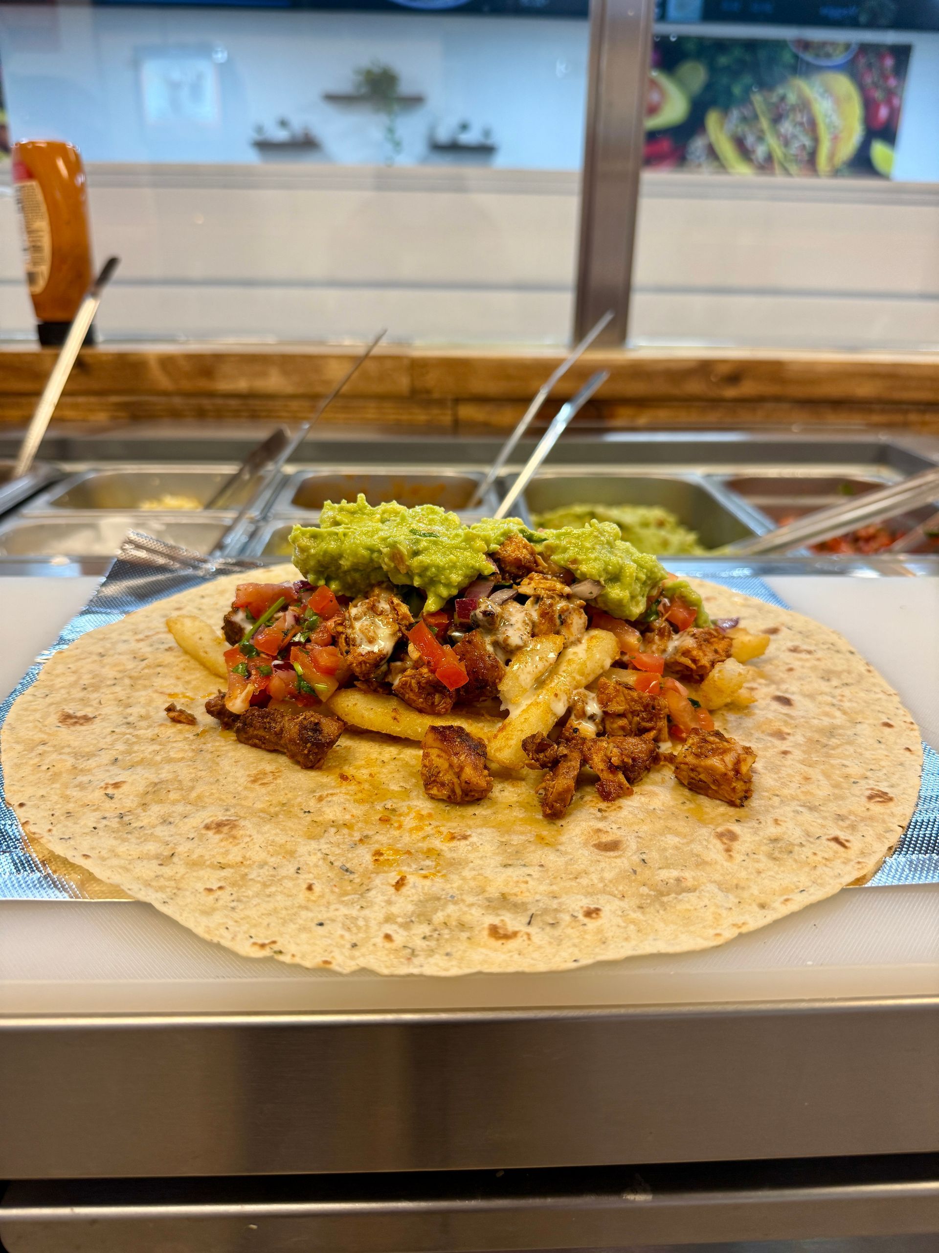 Wrap filled with food, including guacamole, on a stainless steel surface.