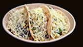 Two tacos topped with shredded cheese on a light-colored plate, set against a dark background.