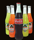 Glass soda bottles: Coca-Cola flanked by four Jarritos fruit sodas, on black background.