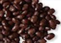 Pile of dark, glossy black beans, close-up view, scattered against a white edge.
