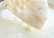 A piece of light-colored food being dipped into a creamy white sauce.