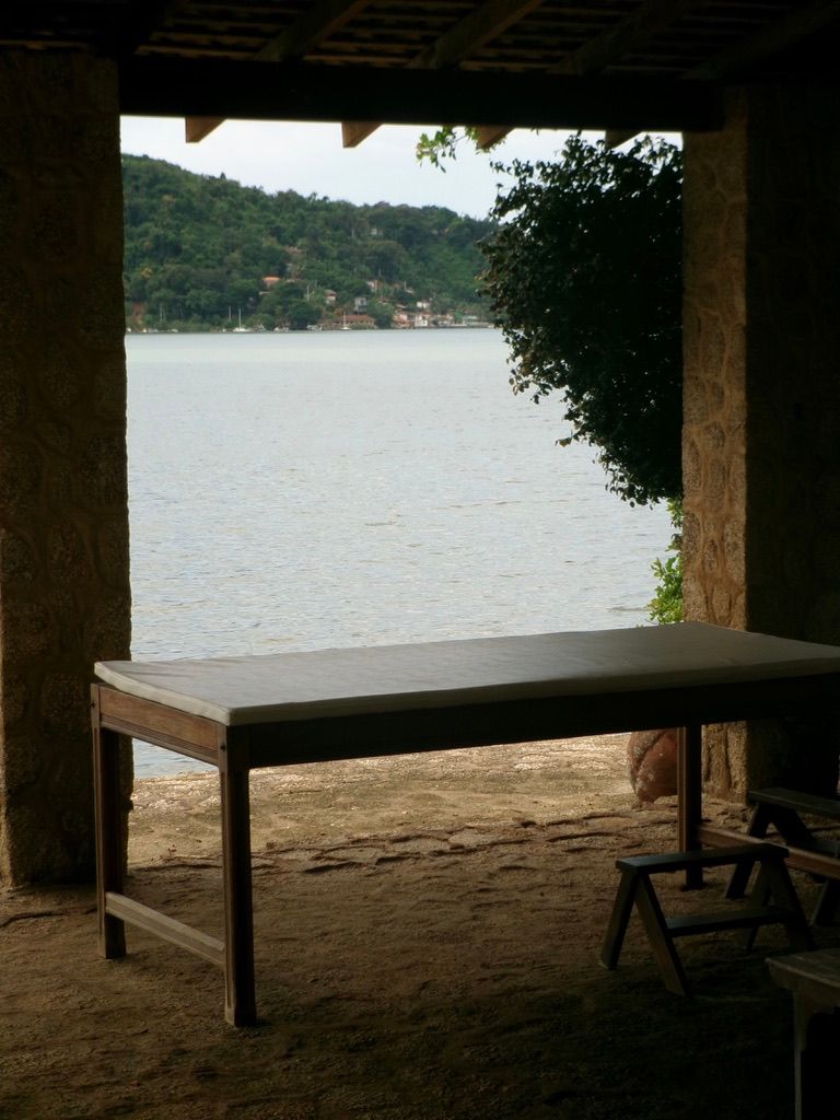 Abrigo coberto à beira do lago com uma mesa de madeira com vista para as águas calmas e colinas verdejantes.
